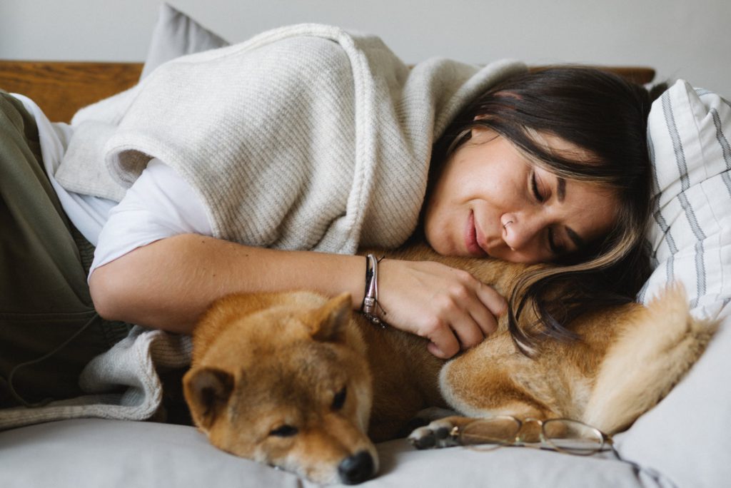 smiling woman and purebred shiba inu dog resting on couch