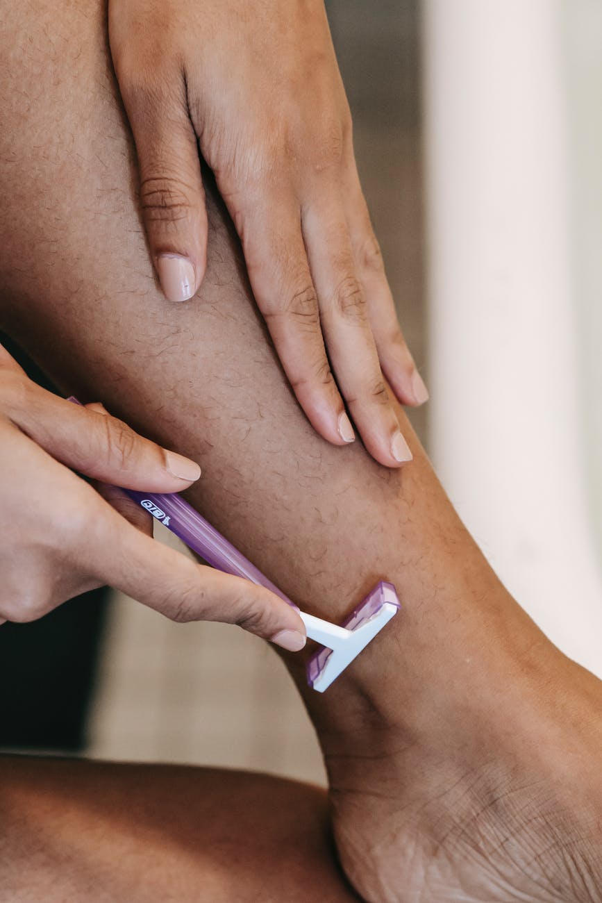 faceless ethnic woman depilating leg with razor