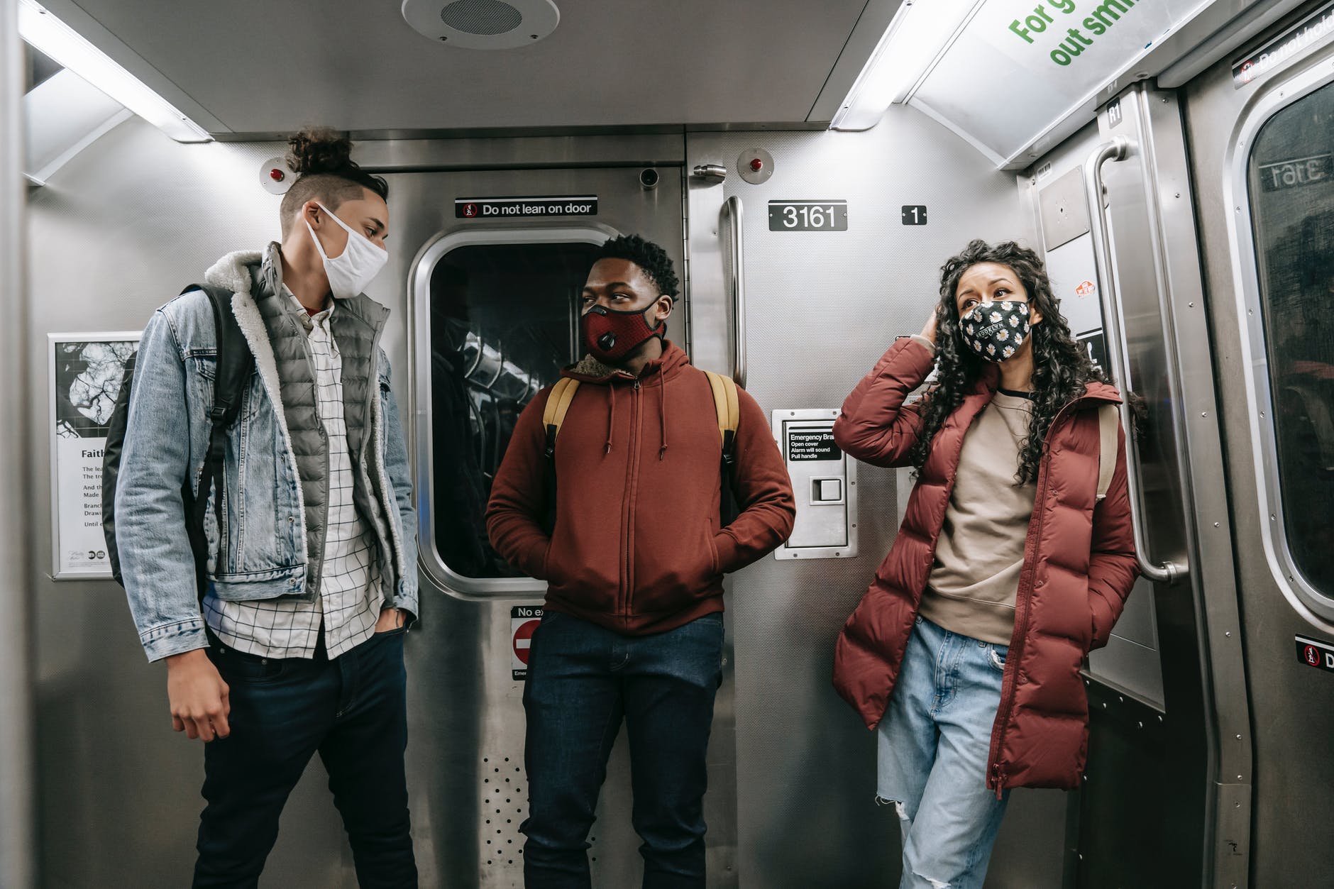 unrecognizable multiethnic friends in masks standing in subway train