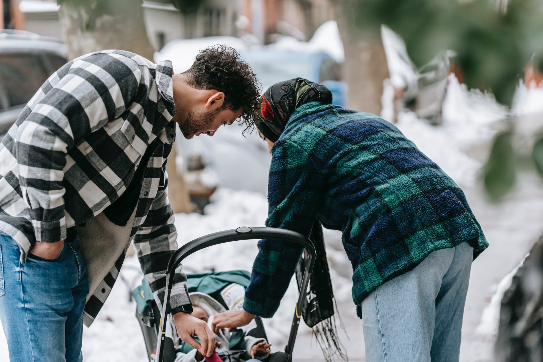ethnic couple bending above small baby in stroller