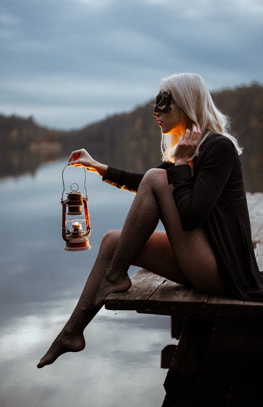 trendy woman with lantern on pier near lake