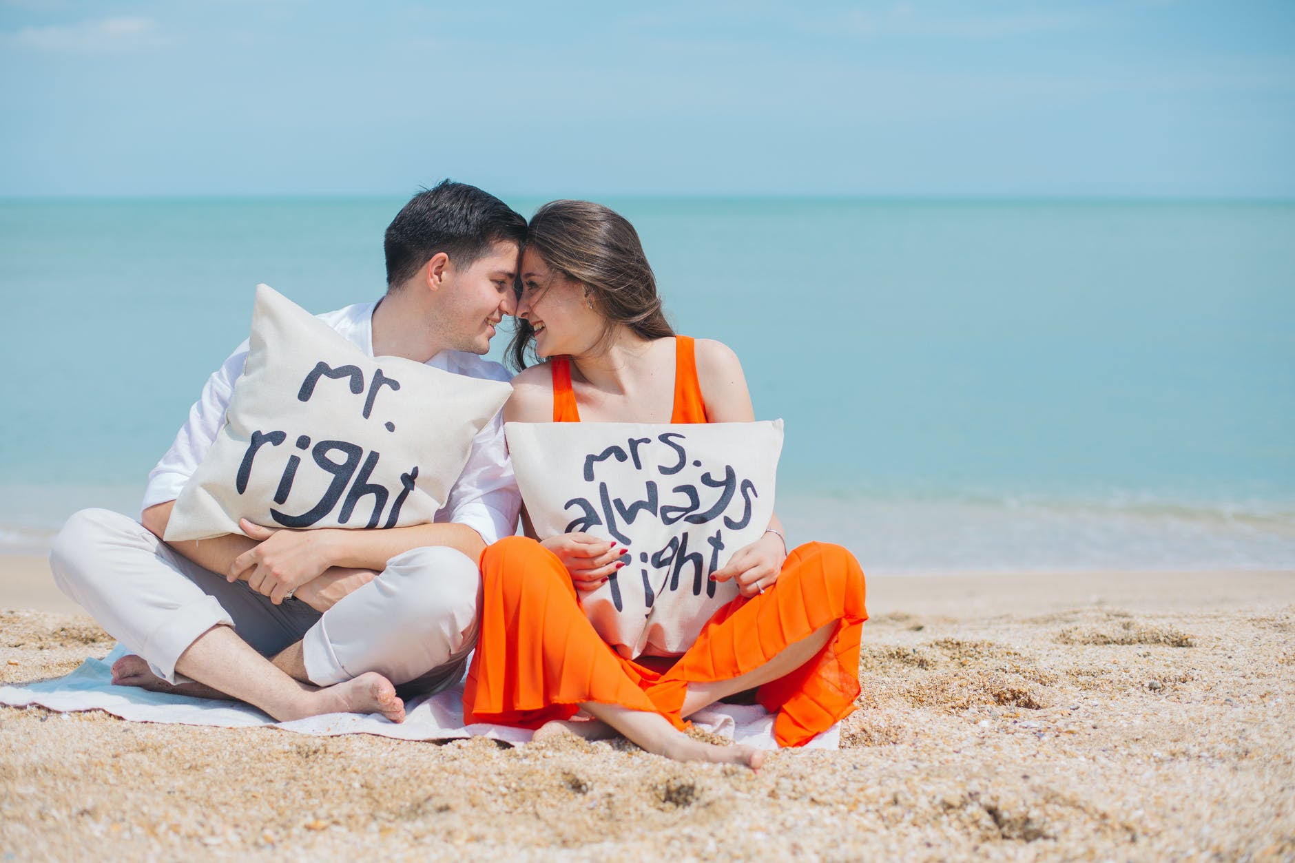 man and woman wearing cloths sitting on brown sand near seashore