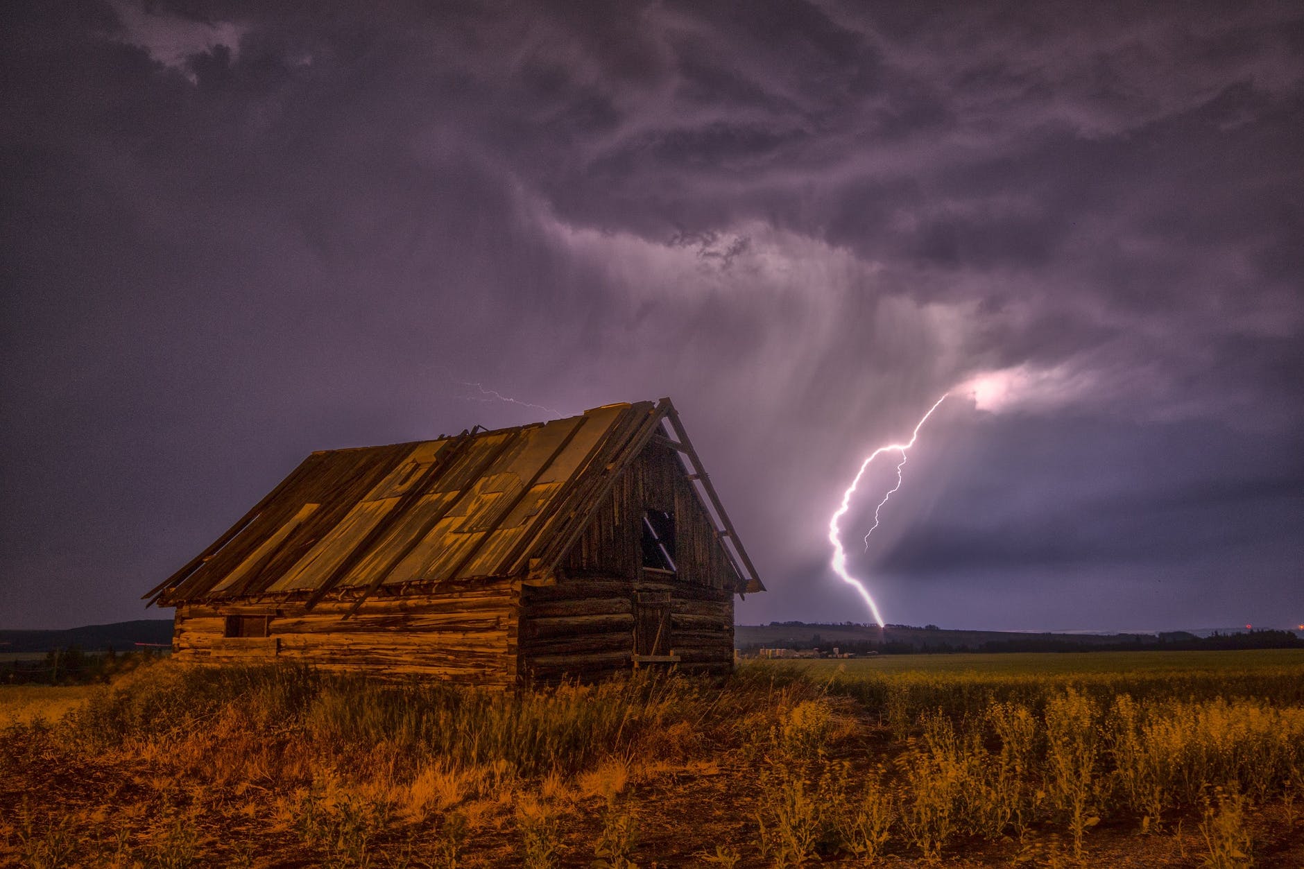 brown and beige wooden barn surrounded with brown grasses under thunderclouds