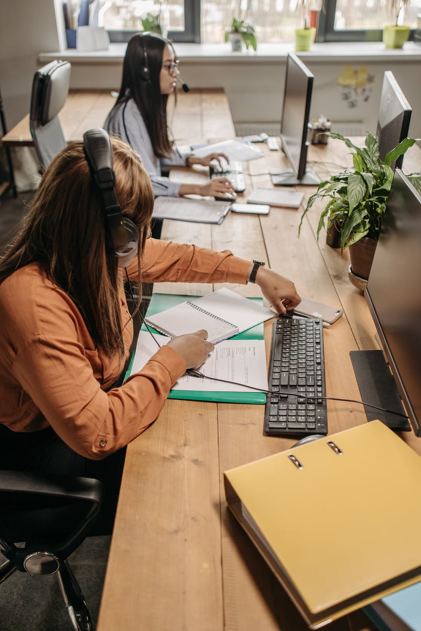 a person with headphones sitting at a desk with a computer and a notebook