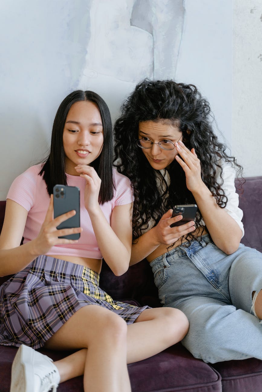 women sitting beside each other while using a phone